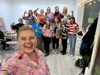 Jungesell:innen Abschied - Teameevent - 12 lachenden, weiblich aussehenden Personen mit Blumenhoop halten ihr Trockenblumen Werkstück in die Kamera während Marleen Jansen, die Workshopleitung das Selfie macht und ebenfalls lacht.