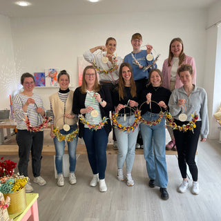10 Frauen im Gruppenbild mit ihren Werkstücken aus dem Trockenblumen Workshop im Südviertel Muenster. Alle lächeln in die Kamera und haben ihre gebastelten Blumenkränze in der Hand.