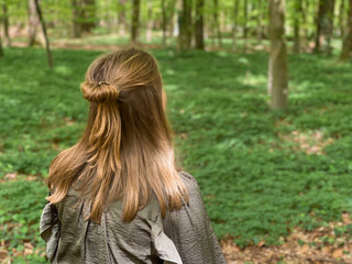 Waldbaden: Person, mit blonden langen Haaren sitzt von hinten im Wald beim Atmen