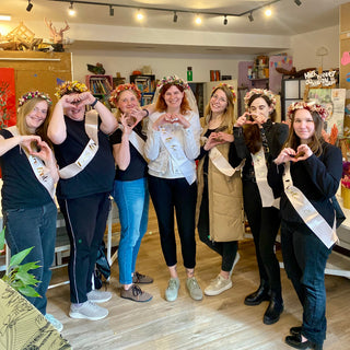 7 Frauen im Gruppenbild mit ihren Werkstücken aus dem Trockenblumen Workshop im Südviertel Muenster. Alle lächeln in die Kamera und haben ihre gebastelten Blumenhaarkränze auf dem Kopf.