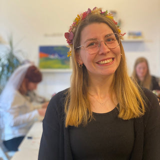 eine Personen mit ihrem Blumenhaarkranz aus dem Trockenblumen Workshop im eigenen Garten. Sie lächelt in die Kamera.