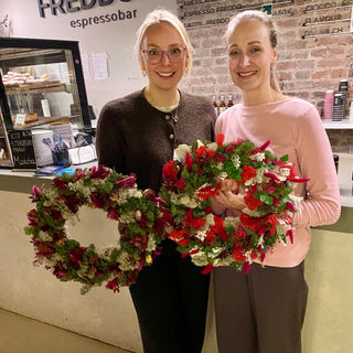 2Frauen halte ihre Adventskränze in der Hand und lächeln in die Kamera beim Adventskranz Workshop in Münster.