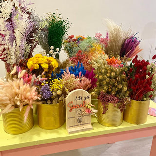 Blumenauswahl bei Blumenworkshop. Es stehen viele bunte, unterschiedliche Trockenblumen auf einem farbigen Tisch. Vorne steht ein Holzschild, auf dem "Let's get special" steht. 