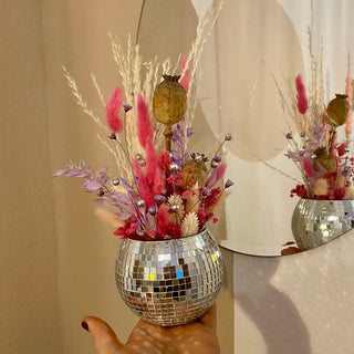 Discokugel Workshop: Vase gefüllt mit gebundeme Strauß aus Trockenblumen. Die Discokugel wird on einer Hand gehalten. Das Wekstück ist exemplarisch für die Discokugeln, die die Teilnehmenden im Kurs in Münster basteln können.  Im Spiegel im Hintergrund sieht man das Werkstück nochmals. 