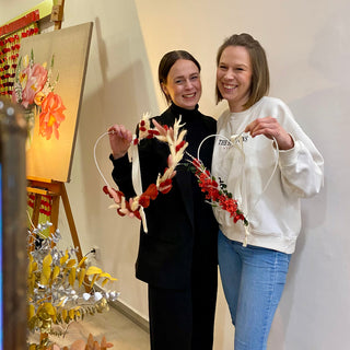 Zwei lachende  Frauen eigen ihre gestalteten Herzhoops mit Trockenblumen in einem DIY Workshop in die Kamera