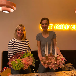 Zwei lachende Frauen halten ihre eigenen gestalteten Adventskränze mit Trockenblumen, Moos und Kerzen in einem DIY Workshop in die Kamera. Diese sind Beispielexemplare für den Blumen-Adventskranz-Workshop mit Trockenblumen in Münster.