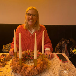 Eine lachende Frau hält ihren eigenen gestalteten Adventskranz mit Trockenblumen, Moos und Kerzen in einem DIY Workshop in die Kamera. Diese sind Beispielexemplare für den Blumen-Adventskranz-Workshop mit Trockenblumen in Münster.