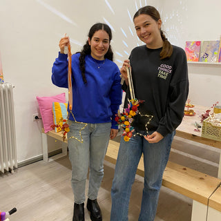 Zwei lachende Frauen halten ihre eigenen gestalteten Sternhoops aus Metall mit farbenfrohen Trockenblumen in einem DIY Workshop in die Kamera. Diese sind Beispielexemplare für den weihnachtliche Sternhoop-Workshop mit Trockenblumen in Münster.