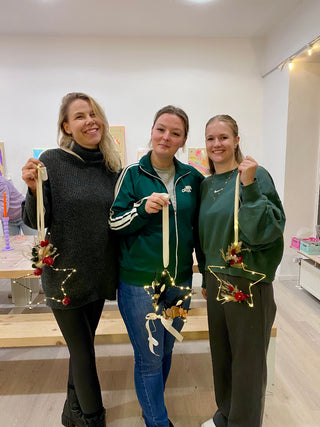 Drei lachende Frauen halten ihre eigenen gestalteten Sternhoops aus Metall mit farbenfrohen Trockenblumen in einem DIY Workshop in die Kamera. Diese sind Beispielexemplare für den weihnachtliche Sternhoop-Workshop mit Trockenblumen in Münster.
