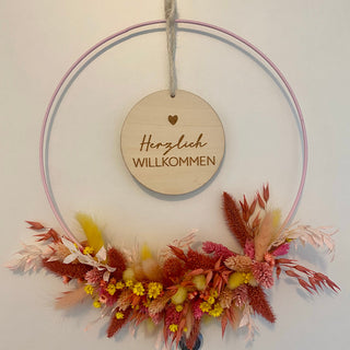 DIY Blumenkranz Workshop – exemplarisches Bild eines im Workshop gebastelten Trockenblumenkranz mit Sommerblumen auf weißem Hintergrund auf dünner, Juteschnur hängend mit mittig hängendem Holzschild mit der Aufschrift Herzlich Willkommen.