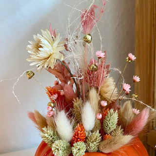 Kürbis ist zu sehen in verschiedenen Orangetönen dekoriert mit gelb, rosa,orange, beigen Trockenblumen für einen Workshop im Herbst in Münster. 