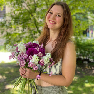 eine Frau mit ihren Werkstück aus dem Trockenblumen Workshop in Muenster. Sie lächelt in die Kamera und hat ihren gebastelten Blumensträuße in der Hand.